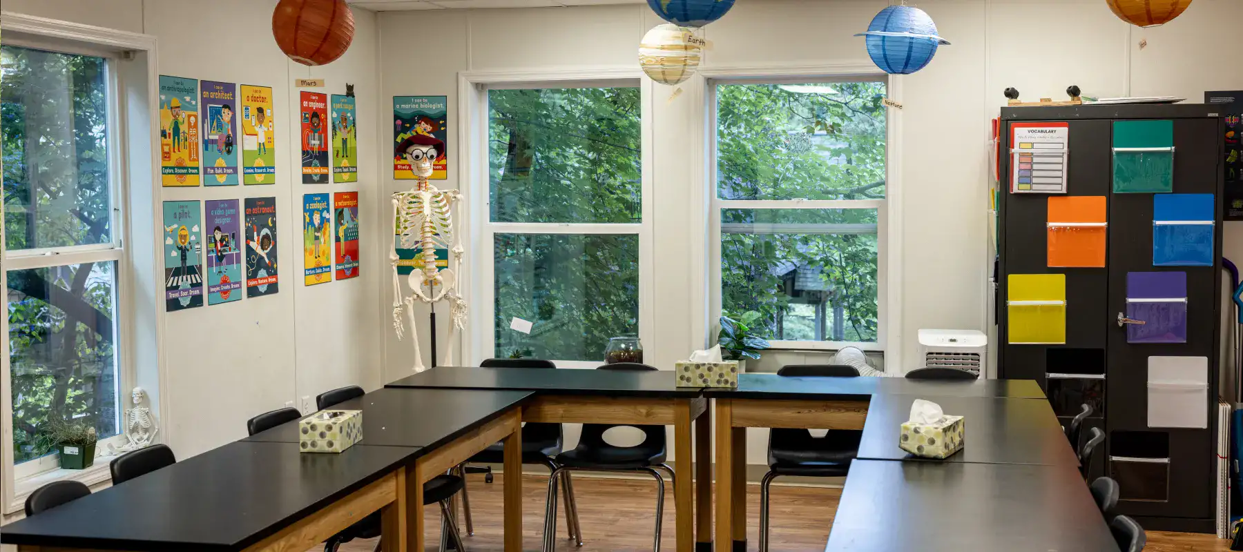 A science classroom with large tables, a skeleton, and several colorful posters and model planets at Lake House Academy accredited therapeutic boarding school.