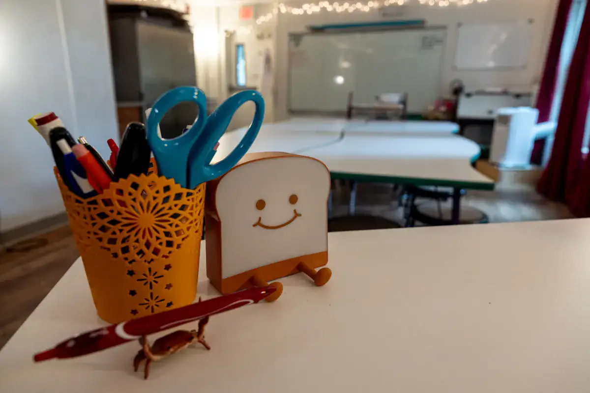 A supply cup and piece of plastic toast with a smiley face on the teacher's desk in a classroom at an accredited therapeutic boarding school.