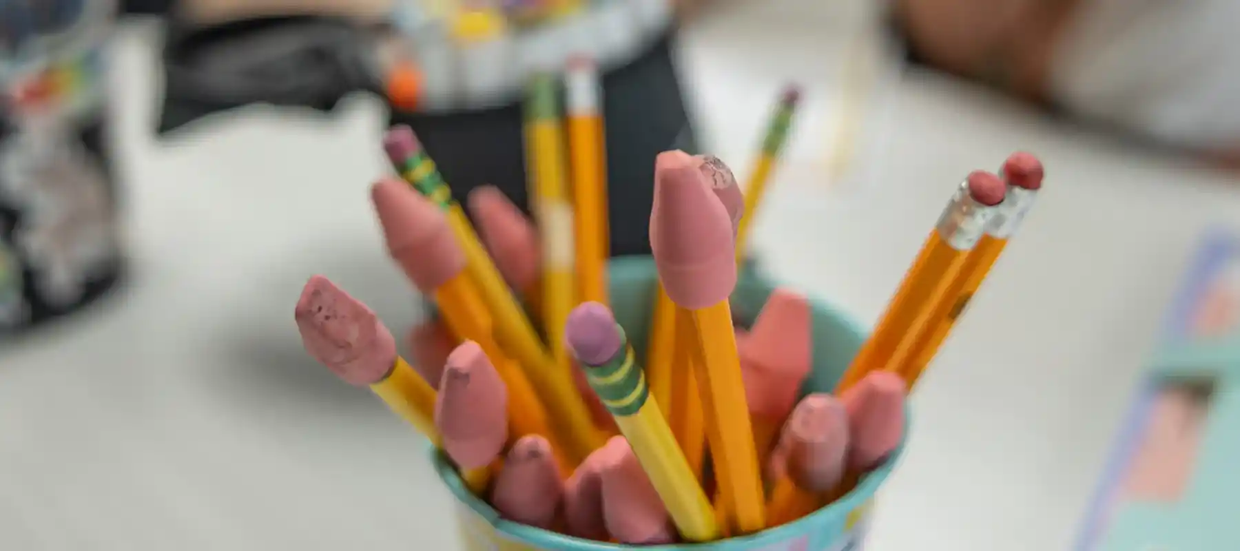 A supply cup full of pencils with erasers sitting a desk with a blurred teacher and student working in the background at an accredited therapeutic boarding school.